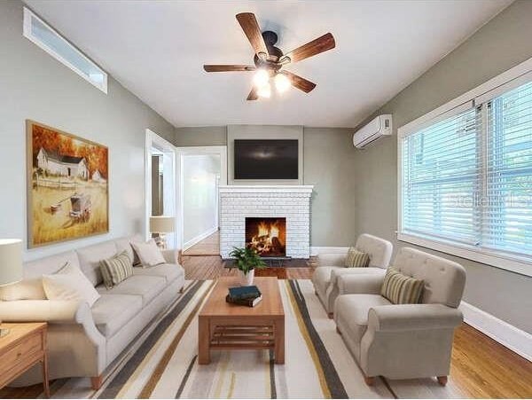 living room with light hardwood / wood-style flooring, a fireplace, an AC wall unit, and ceiling fan