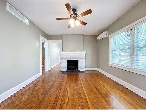 unfurnished living room featuring hardwood / wood-style floors, a fireplace, a wall unit AC, and ceiling fan