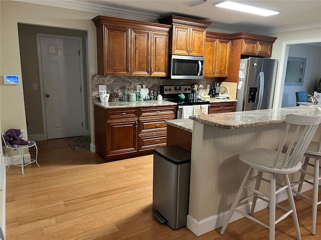 kitchen with ornamental molding, appliances with stainless steel finishes, tasteful backsplash, and a breakfast bar area