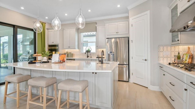 kitchen featuring appliances with stainless steel finishes, a kitchen island with sink, hanging light fixtures, white cabinets, and a kitchen bar