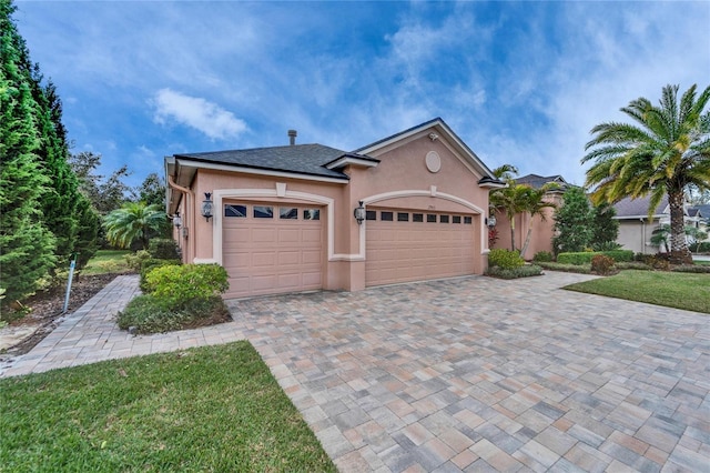 view of front of house featuring decorative driveway, an attached garage, a front yard, and stucco siding