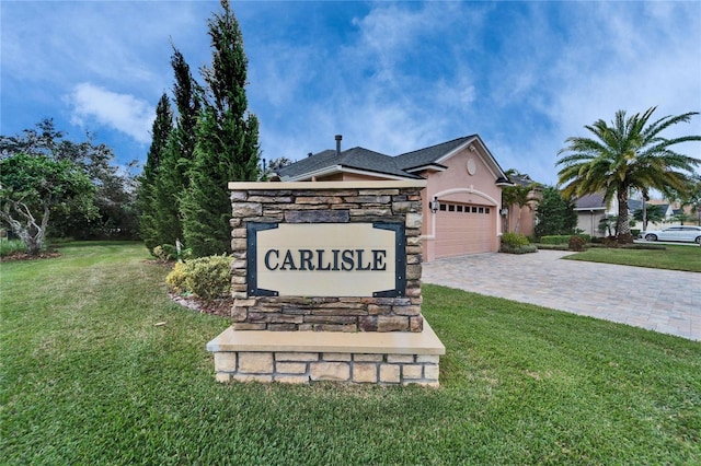 community sign featuring a garage, a yard, and decorative driveway