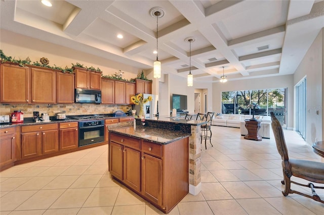 kitchen with dark stone counters, brown cabinetry, a kitchen island, black appliances, and light tile patterned flooring