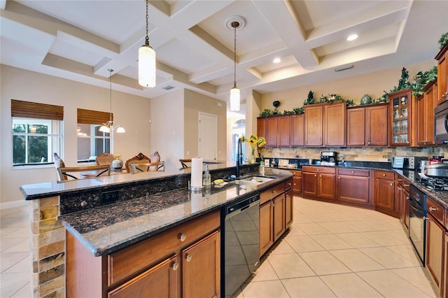 kitchen with an island with sink, sink, backsplash, hanging light fixtures, and black appliances