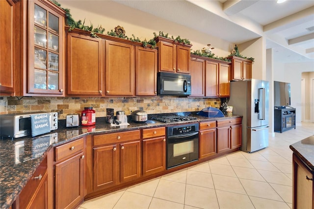 kitchen with tasteful backsplash, glass insert cabinets, light tile patterned flooring, dark stone counters, and black appliances