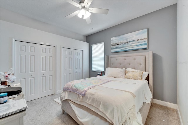 bedroom with a ceiling fan, light colored carpet, baseboards, and two closets