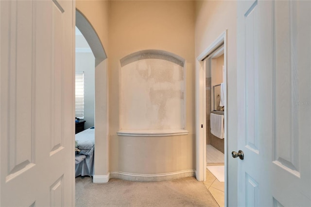 hallway featuring arched walkways, light colored carpet, and baseboards