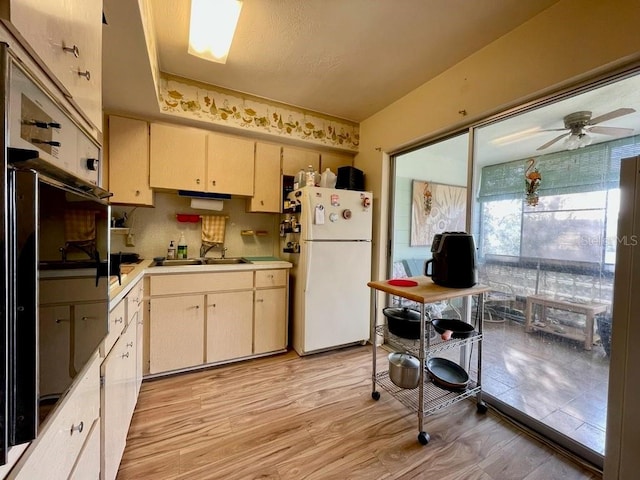 kitchen with light wood-type flooring, cream cabinetry, white refrigerator, sink, and ceiling fan