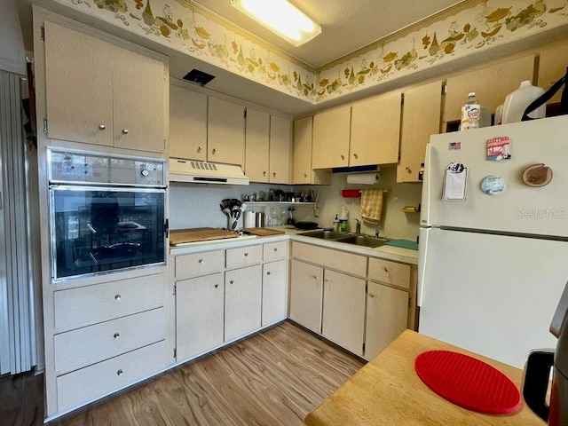 kitchen with light hardwood / wood-style flooring, cooktop, sink, oven, and white fridge