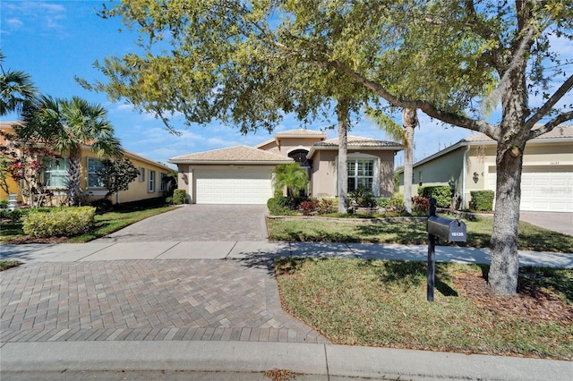 view of front of property featuring a front lawn, a tiled roof, stucco siding, decorative driveway, and an attached garage