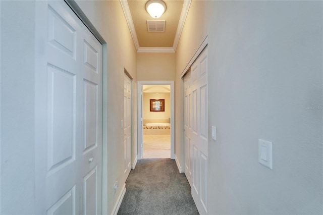 hall with dark colored carpet, visible vents, baseboards, and ornamental molding