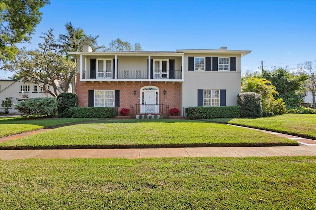 front of property with a balcony, brick siding, stucco siding, a front lawn, and a chimney