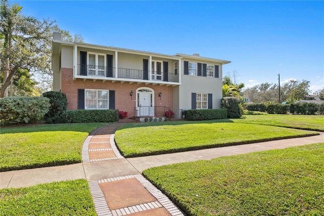 view of front of home featuring a balcony, brick siding, stucco siding, a chimney, and a front yard