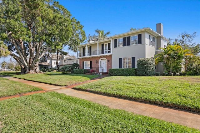 view of front of property featuring a balcony, stucco siding, a chimney, a front lawn, and brick siding