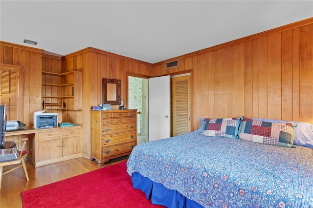 bedroom featuring crown molding, light wood-style flooring, visible vents, and wooden walls