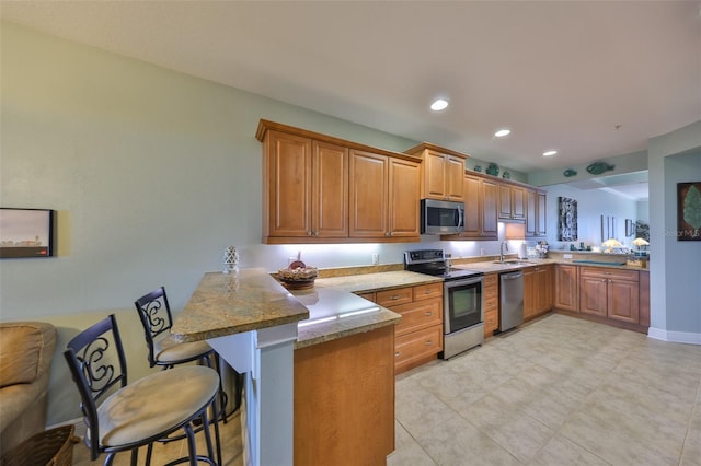 kitchen with sink, appliances with stainless steel finishes, a kitchen breakfast bar, kitchen peninsula, and light stone countertops