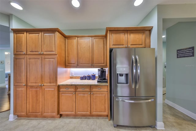 kitchen featuring light stone counters, vaulted ceiling, and stainless steel fridge with ice dispenser