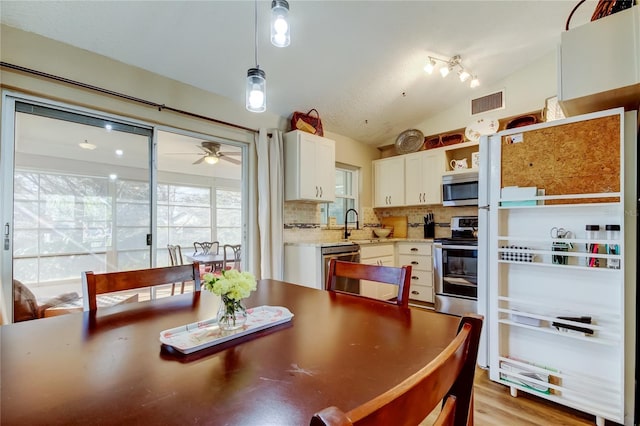 kitchen with lofted ceiling, appliances with stainless steel finishes, white cabinetry, decorative backsplash, and decorative light fixtures