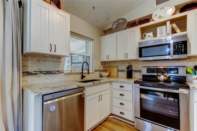 kitchen featuring sink, light stone counters, vaulted ceiling, appliances with stainless steel finishes, and white cabinets