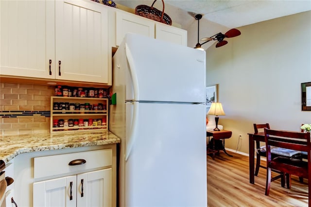 kitchen featuring white fridge, light stone counters, white cabinets, and backsplash