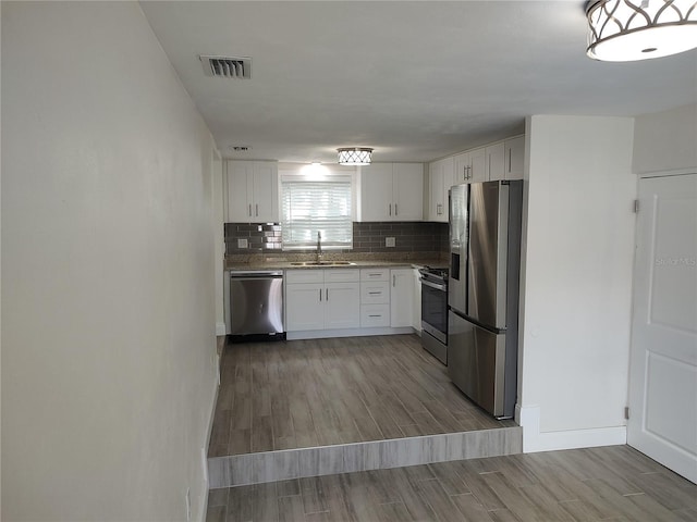 kitchen featuring visible vents, backsplash, appliances with stainless steel finishes, a sink, and wood finished floors