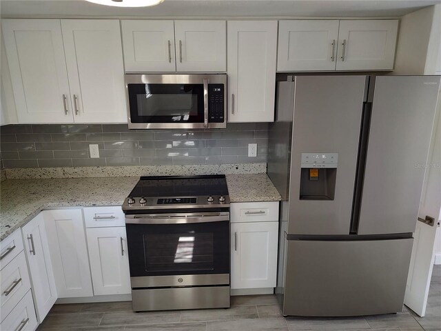 kitchen with light stone countertops, white cabinetry, stainless steel appliances, and backsplash