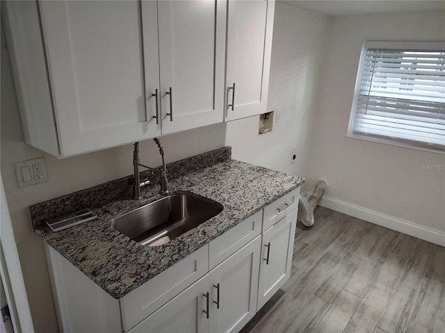 kitchen featuring stone countertops, a sink, white cabinetry, baseboards, and light wood-type flooring