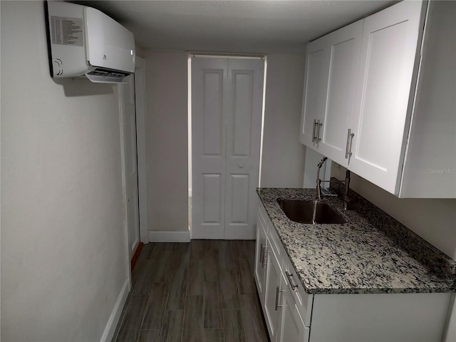 kitchen featuring stone counters, dark wood-style floors, white cabinetry, a sink, and a wall mounted air conditioner