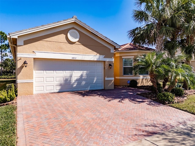 ranch-style house featuring a garage, decorative driveway, a tile roof, and stucco siding