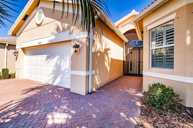 view of side of home featuring decorative driveway, an attached garage, and stucco siding