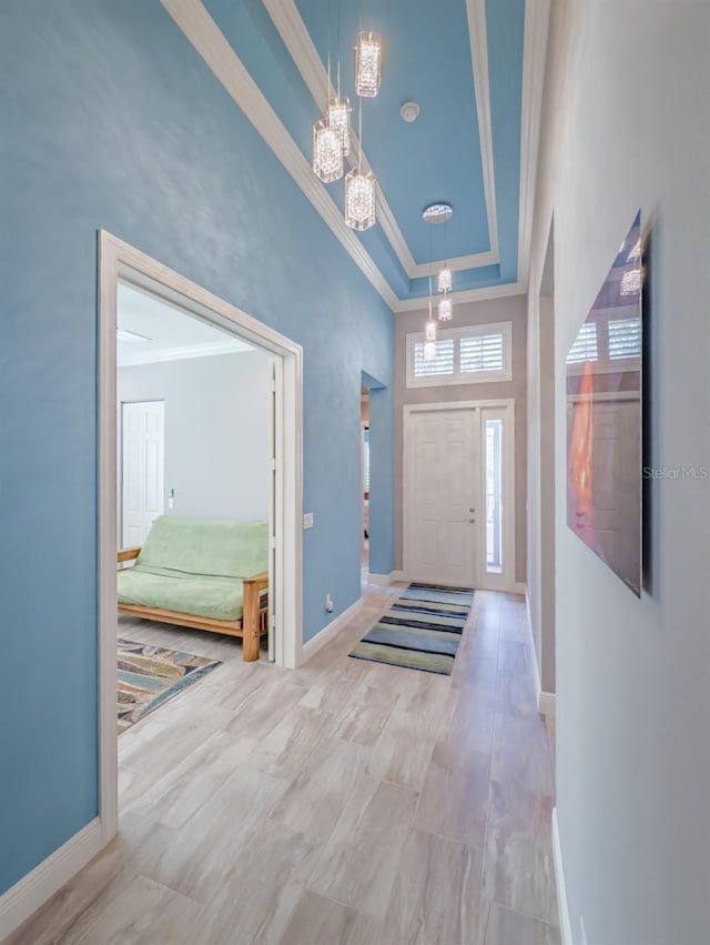 entrance foyer featuring ornamental molding, a tray ceiling, a high ceiling, and baseboards