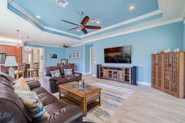 living room with visible vents, baseboards, ceiling fan, a tray ceiling, and crown molding