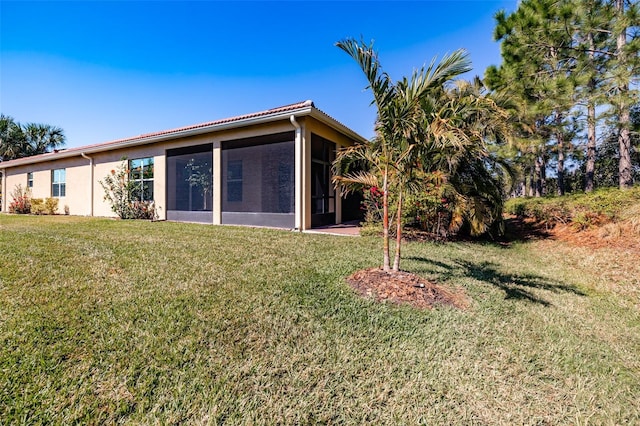 back of house featuring a sunroom, stucco siding, and a yard