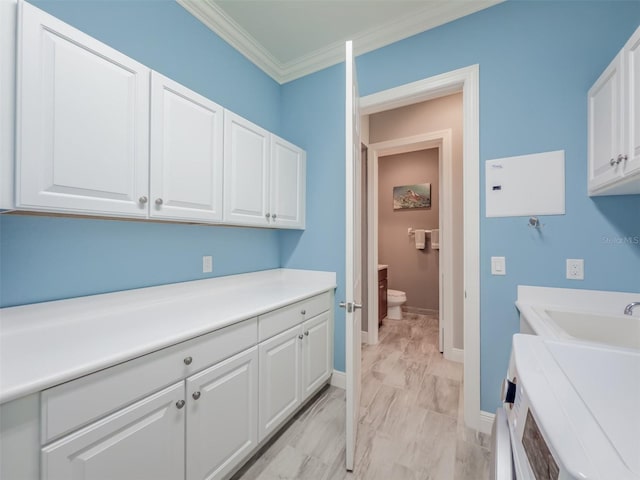 clothes washing area featuring cabinet space, washer / dryer, baseboards, crown molding, and a sink