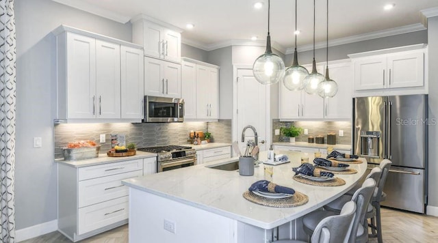 kitchen featuring pendant lighting, high quality appliances, an island with sink, sink, and white cabinets