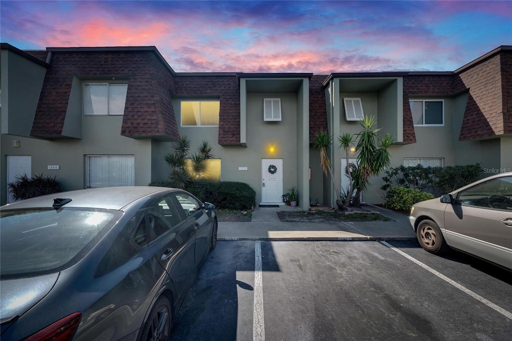 townhome / multi-family property featuring uncovered parking, mansard roof, and roof with shingles