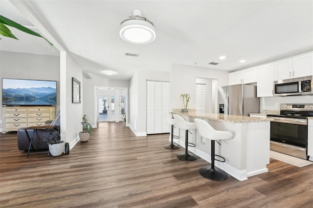 kitchen with light stone counters, white cabinetry, a kitchen island, stainless steel appliances, and a breakfast bar area