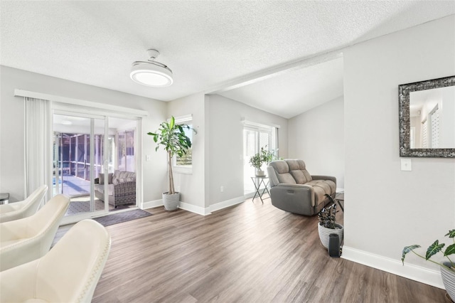 living area with a textured ceiling, hardwood / wood-style flooring, and vaulted ceiling