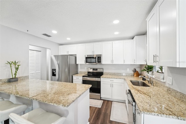 kitchen featuring appliances with stainless steel finishes, sink, light stone counters, white cabinetry, and a breakfast bar area