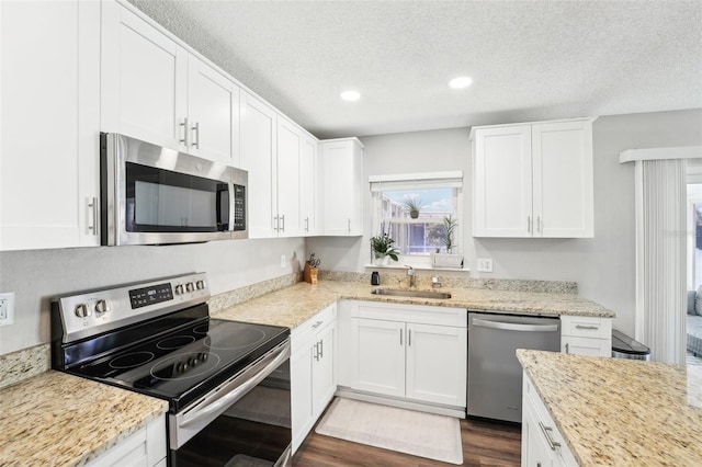 kitchen with white cabinetry, stainless steel appliances, light stone counters, and sink