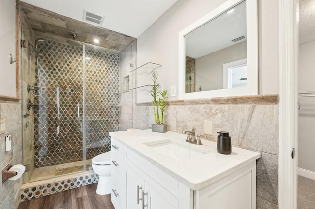 bathroom with tile walls, vanity, toilet, and a shower with shower door