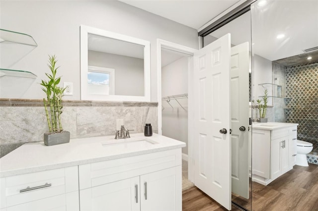 bathroom with a tile shower, tile walls, toilet, wood-type flooring, and vanity