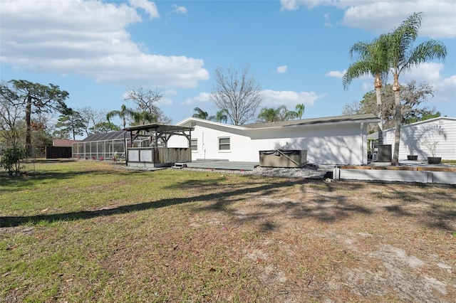 back of property with a hot tub, glass enclosure, and a lawn