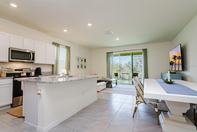 kitchen with white cabinetry, light tile patterned floors, light stone counters, stainless steel appliances, and a center island with sink