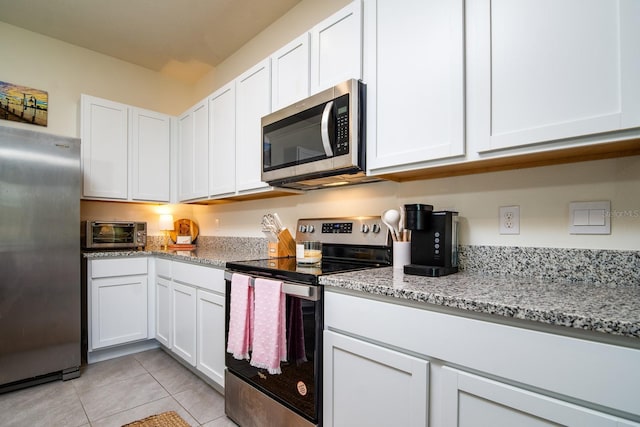 kitchen with light tile patterned flooring, appliances with stainless steel finishes, light stone countertops, and white cabinets