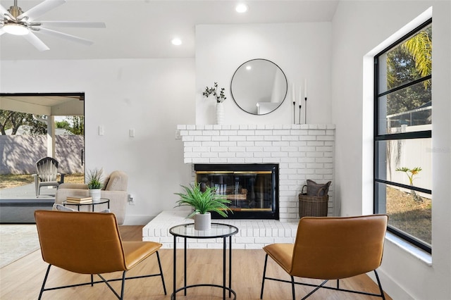 living area with ceiling fan, a wealth of natural light, a fireplace, and light hardwood / wood-style floors