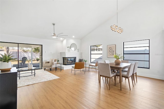 dining room with ceiling fan, a fireplace, high vaulted ceiling, and light wood-type flooring