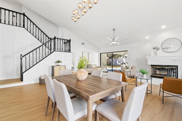 dining space with lofted ceiling, ceiling fan with notable chandelier, a fireplace, and light hardwood / wood-style flooring