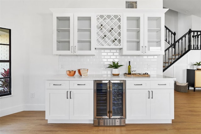 bar with light hardwood / wood-style flooring, light stone countertops, beverage cooler, and white cabinets