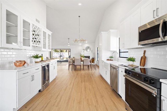 kitchen featuring appliances with stainless steel finishes, pendant lighting, white cabinets, wine cooler, and light hardwood / wood-style floors